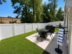 A patio with a table and chairs, a grill, and a white fence. - Coastal Clubhouse | Beach + Golf + Putting green (North Myrtle Beach)