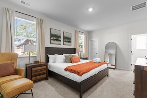 A modern bedroom with a large bed, bedside tables, a chair, and artwork on the wall. - Coastal Clubhouse | Beach + Golf + Putting green (North Myrtle Beach)