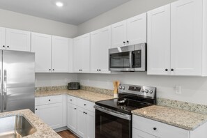 A modern kitchen with white cabinets, stainless steel appliances, and granite countertops. - Coastal Clubhouse | Beach + Golf + Putting green (North Myrtle Beach)