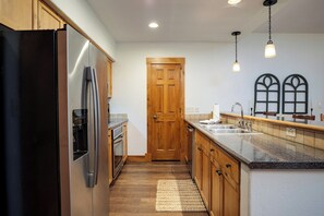 A modern kitchen with wooden cabinets, a stainless steel refrigerator, an oven, a sink, and a granite countertop. - TL2101 | Inviting Mountain Style | Beautiful Décor | Hot Tubs | A/C (Steamboat Springs)