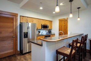 Eine moderne Küche mit Holzausstattung, Edelstahlgeräten, einer eingebauten Mikrowelle und einer Bar mit Barhocker.