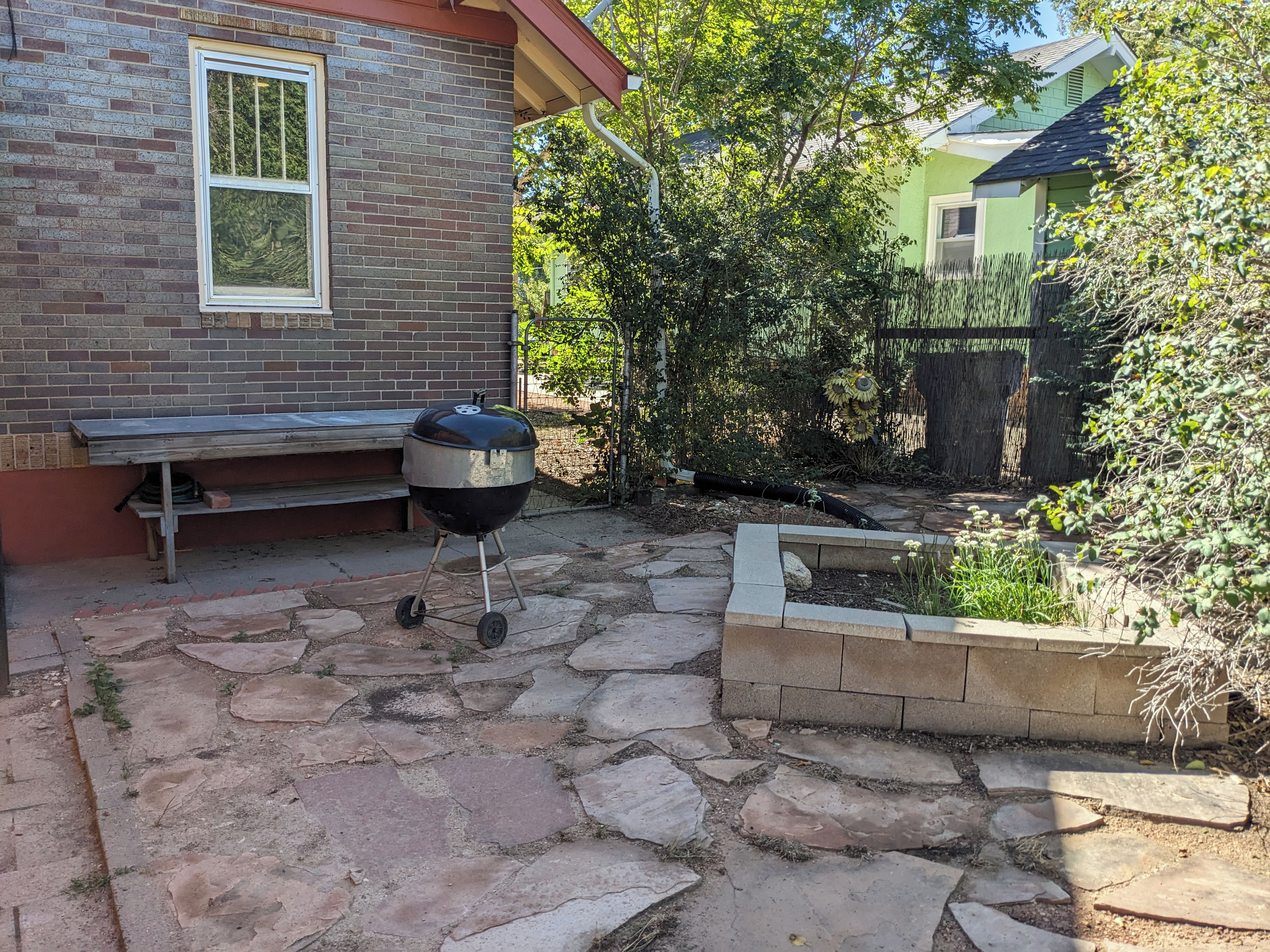 A stone patio with a barbecue grill, a wooden bench, and a brick wall.