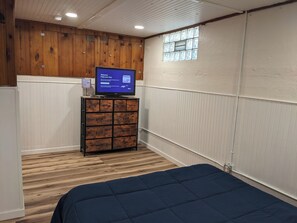Ein Zimmer mit einem Bett, einem Holfachschrank mit Fernseher und einem Fenster.