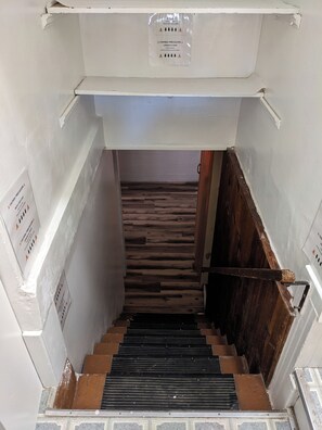 A staircase with a wooden floor and a metal handrail, leading to a room with white walls and a caution sign. - Charming 3BR/2BA Craftsman near Hospitals - Yard & BBQ (Pueblo)