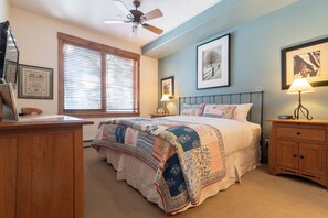 Ein Schlafzimmer mit einem Bett, Nachttischen aus Holz, einem Schreibtisch und einem Deckenventilator.
