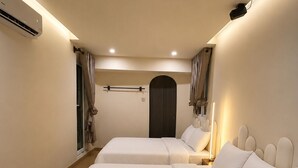 Une chambre d’hôtel avec deux lits, une porte sombre et un luminaire au plafond.