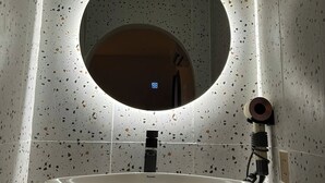 Une salle de bain avec un lavabo sur pied, un miroir rond et des carreaux muraux à motifs.