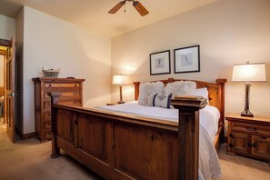 Een slaapkamer met een houten bed, twee nachtkastjes met lampen, een houten dressoir, en twee ingelijste foto's aan de muur.