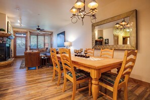 A dining area with a wooden table, chairs, and a chandelier. There is a fireplace, a sofa, and a window with blinds. - TL2103 | Easy Access to Slopes | Beautiful Décor | Winter Shuttle | Hot Tubs (Steamboat Springs)