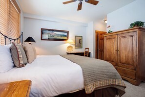 Een slaapkamer met een bed, een houten garderobe, een bureau met een lamp en een aan de muur hangend schilderij.