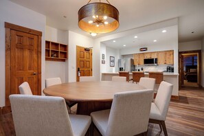 Un'ampia sala da pranzo con un grande tavolo rotondo e sei sedie, una cucina con mobili in legno e elettrodomestici moderni, e un lampadario a soffitto.