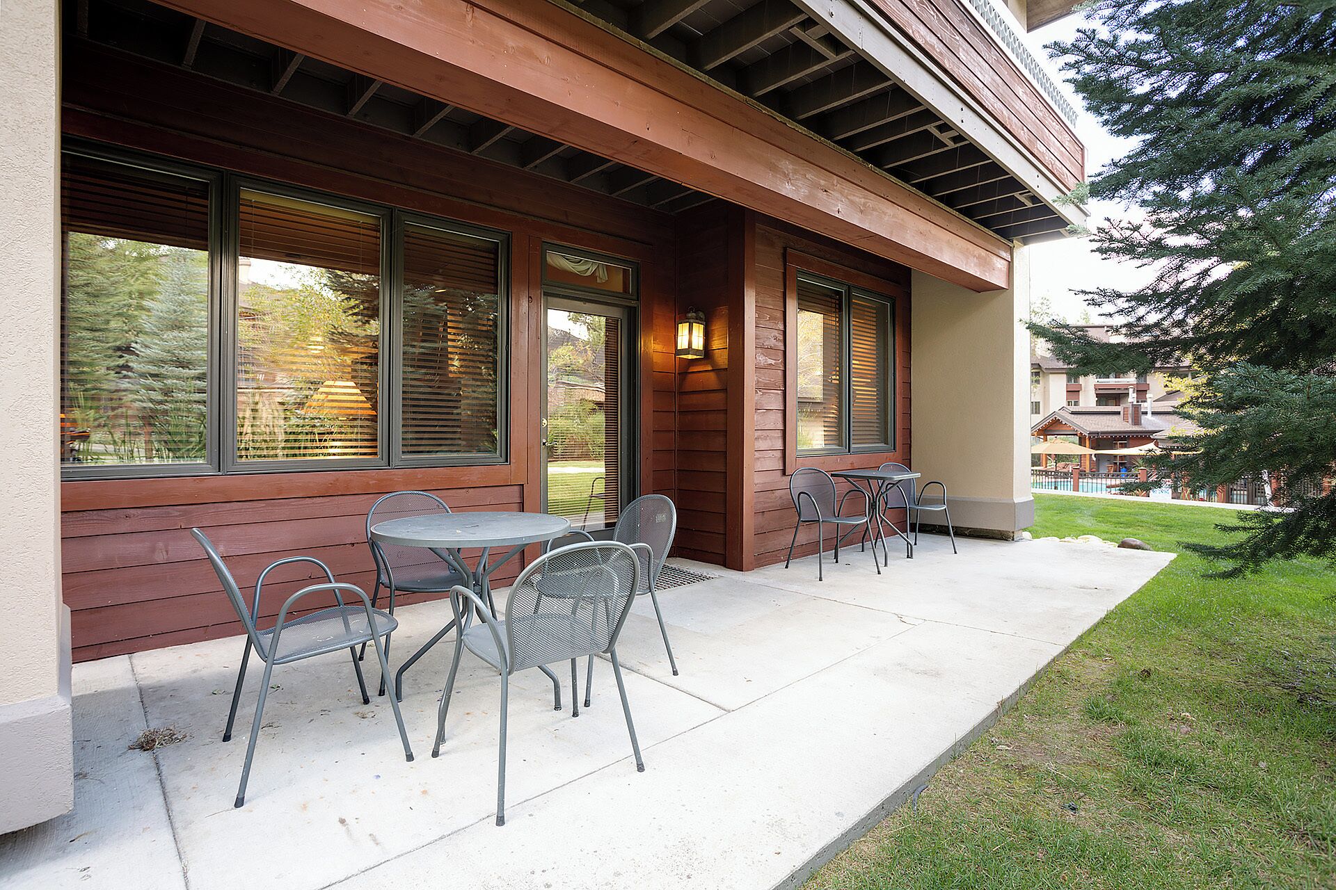 An outdoor patio with metal chairs and a table, wooden siding, and large windows.