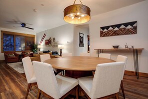 A spacious living room with a large wooden dining table surrounded by white upholstered chairs, a ceiling fan, and a modern chandelier. - TL2108 | Beautiful Mountain Condo | Prime location | A/C | Hot Tubs (Steamboat Springs)