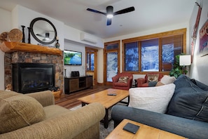 A cozy living room with a fireplace, comfortable seating, and large windows with blinds. - TL2108 | Beautiful Mountain Condo | Prime location | A/C | Hot Tubs (Steamboat Springs)