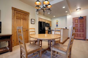 A dining area with a round wooden table and four chairs, a black refrigerator, wooden cabinets, and a chandelier. - TL2110 | Perfect Getaway | Winter Shuttle | 10 Hot Tubs | Private Patio (Steamboat Springs)