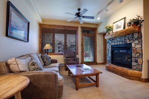 A cozy living room with a fireplace, a ceiling fan, and a large window with blinds. - TL2110 | Perfect Getaway | Winter Shuttle | 10 Hot Tubs | Private Patio (Steamboat Springs)