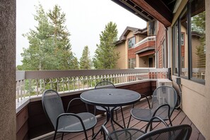 Ein Balkon mit rundem Tisch und vier Stühlen, mit Blick auf eine Wohngegend mit Bäumen und einem Haus.