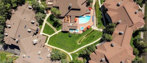 Aerial view of a residential property complex featuring a central swimming pool, manicured lawns, and private outdoor spaces surrounded by villa-style accommodations and lush landscaping.