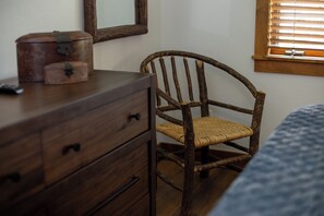 Una silla de madera rústica con asiento tejido, un aparador de madera con cajones y un espejo en la pared.