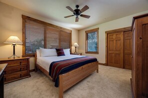 Ein Schlafzimmer mit einem hölzernen Bett, zwei Nachttischen inklusive Lampen, einem Deckenventilator und einer Holztür.