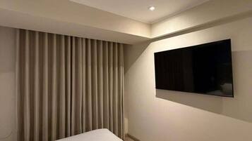 A hotel room with a bed, a wall-mounted TV, and a window with curtains.