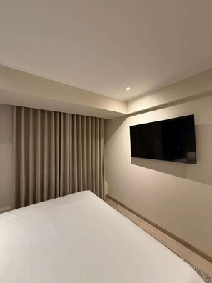 Ein Hotelzimmer mit einem Bett, einem an der Wand befestigten Fernseher und einem Fenster mit Vorhängen.