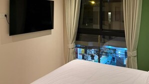 Ein Hotelzimmer mit einem Bett, einem an der Wand befestigten Fernseher und einem Fenster mit Vorhängen.