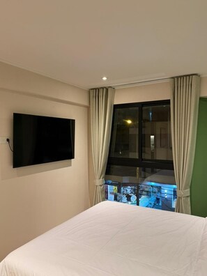 Ein Hotelzimmer mit einem Bett, einem an der Wand befestigten Fernseher und einem Fenster mit Vorhängen.