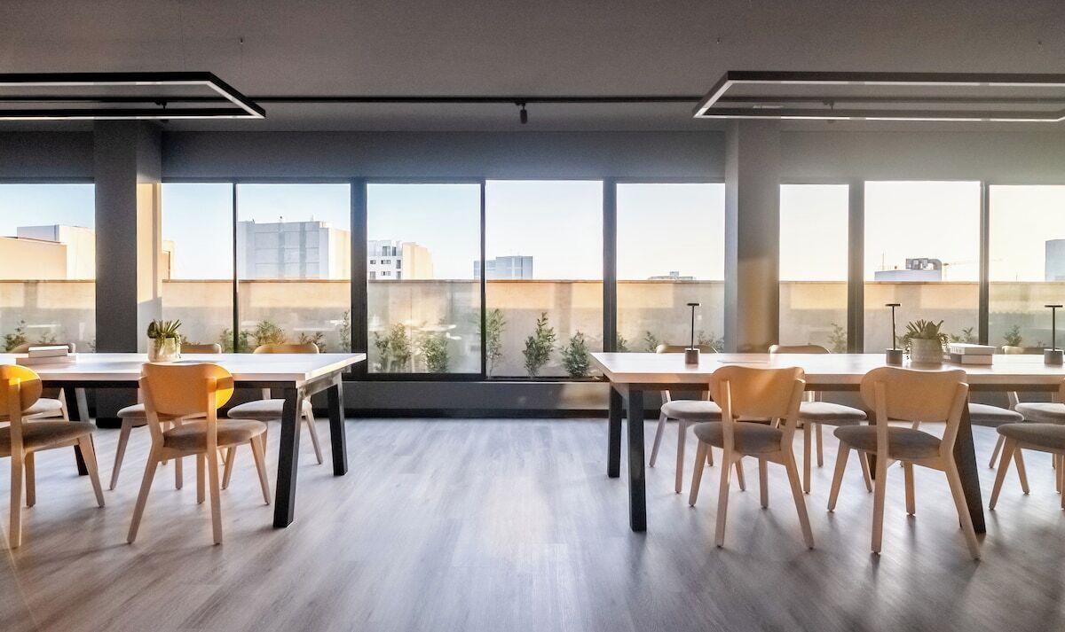 A modern conference room with large windows, wooden tables, and chairs.