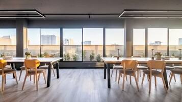 A modern conference room with large windows, wooden tables, and chairs.