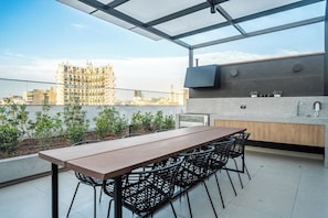Eine Terrassenanlage im Freien mit Esstisch und Stühlen, einer integrierten Küchenzeile und Blick auf die Stadt.