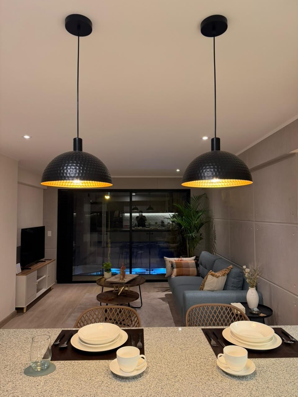 Una sala de estar moderna con sofá, mesa de comedor y lámparas colgantes.
