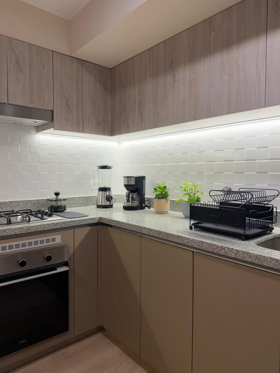 Una cocina moderna con estufa a gas empotrada, electrodomésticos de acero inoxidable y salpicadero de azulejos blancos.