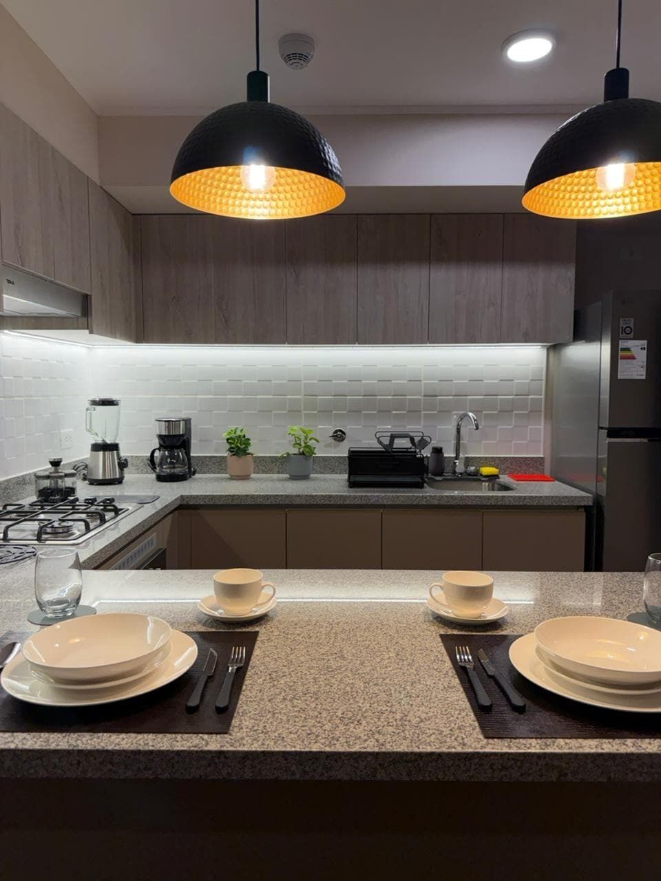 A modern kitchen with two pendant lights, a gas stove, a coffee maker, and a refrigerator.