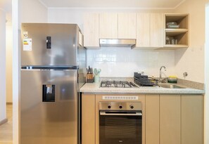 Een compacte keuken met een roestvrijstalen koelkast, een ingebouwde oven en een gasfornuis.