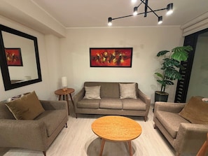 Ein Wohnzimmer mit einer Sofagarnitur, einem runden Couchtisch, einer Zimmerpflanze und einem Bild an der Wand.