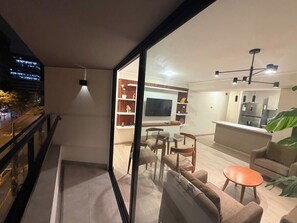 A modern living room with a glass partition, a dining area, a kitchen, and a balcony with a view of the city. - Larco Av. | Balcony · Pool · Gym · Miraflores (Miraflores)