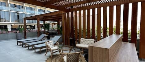 An outdoor seating area with lounge chairs, a wooden table, and a pergola structure.
