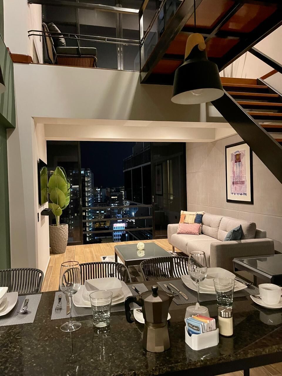 Un comedor moderno con vista a la ciudad, un sofá y una mesa de comedor preparada para dos personas.