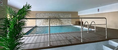 Une piscine intérieure dotée d’une terrasse en bois, de rampes en métal et d’une plante en pot.