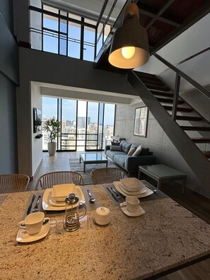 A modern kitchen with a dining area, large windows, and a staircase. - Elegant Duplex with Terrace Sea View (Miraflores)