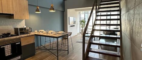 Une cuisine moderne avec un îlot central en bois, un coin repas et un escalier menant à un niveau supérieur.