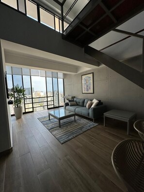 A spacious living area with a large window, a sofa, a coffee table, and a staircase. - Elegant Duplex with Terrace Sea View (Miraflores)