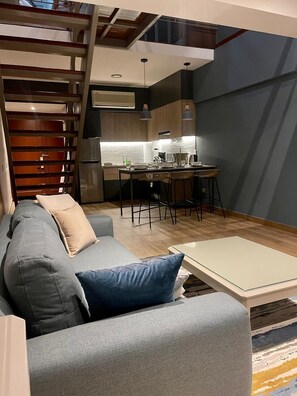 A modern living room with a sofa, a coffee table, and a kitchen area with a dining table and chairs. - Elegant Duplex with Terrace Sea View (Miraflores)