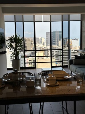 A dining area with a city view, a potted plant, and a modern kitchen setup. - Elegant Duplex with Terrace Sea View (Miraflores)