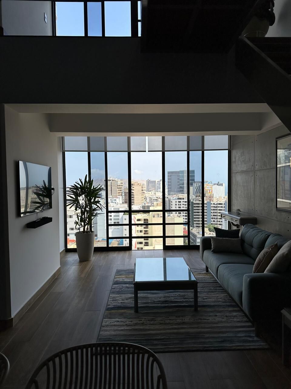 A modern living room with a large window, a sofa, a coffee table, and a potted plant.