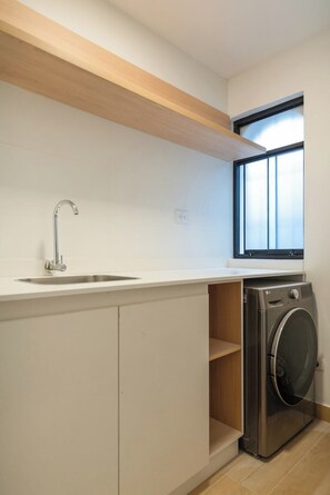 Eine kompakte Küche mit Spüle, Fenster über der Arbeitsfläche und Waschmaschine in der Ecke.