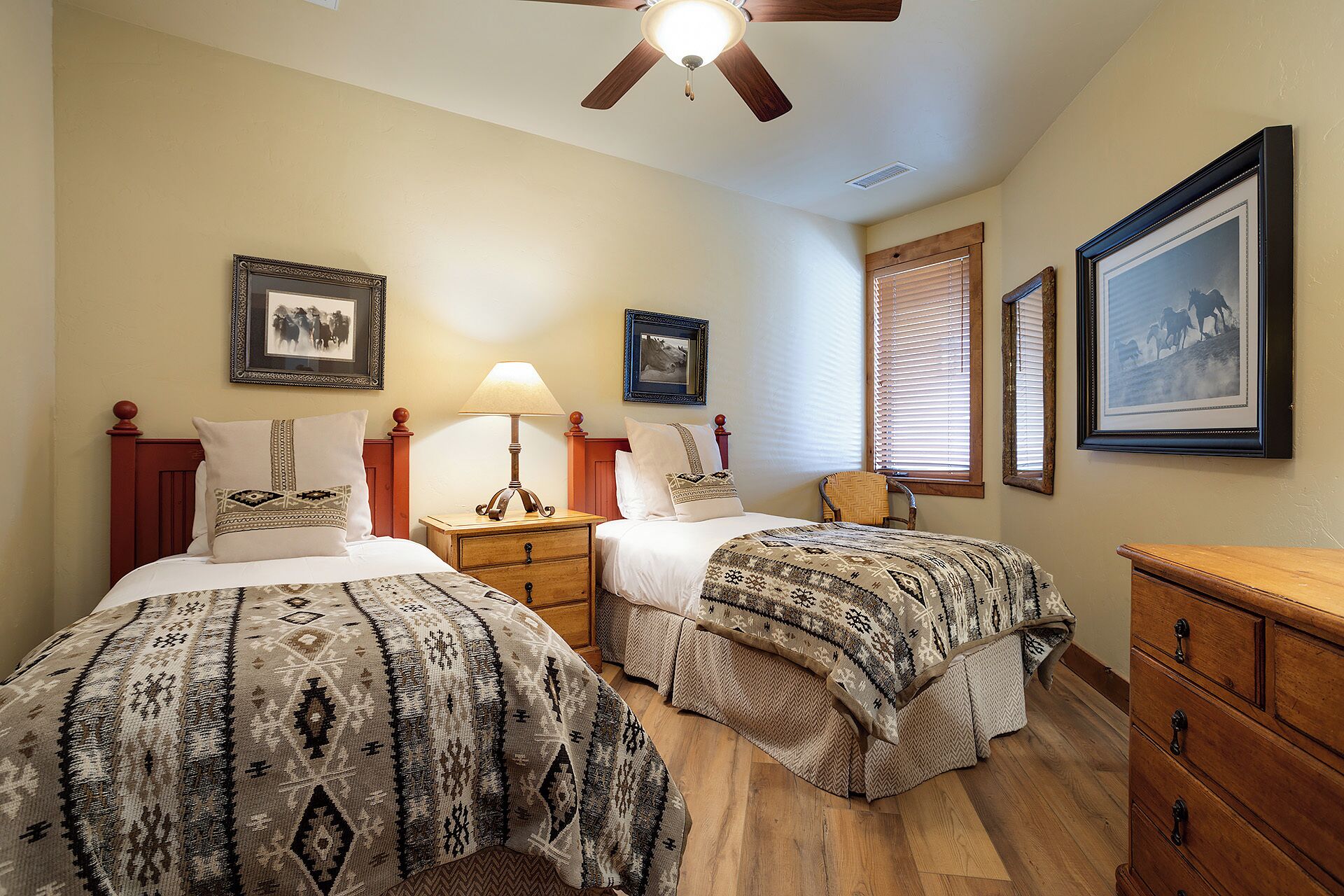 A hotel room with two beds, a wooden dresser, a ceiling fan, and framed pictures on the walls.