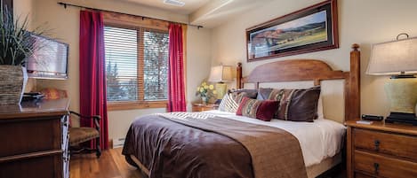 Ein Schlafzimmer mit einem großen Bett, einem Holzkopfende, Nachttischen, einem Deckenventilator und einem Fenster mit Jalousien.