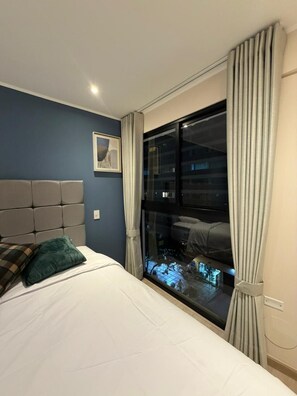 A hotel room with a bed, a headboard, a window with curtains, and a framed picture on the wall. - Boutique 2BR in Miraflores | Pool · Gym · BBQ (Miraflores)
